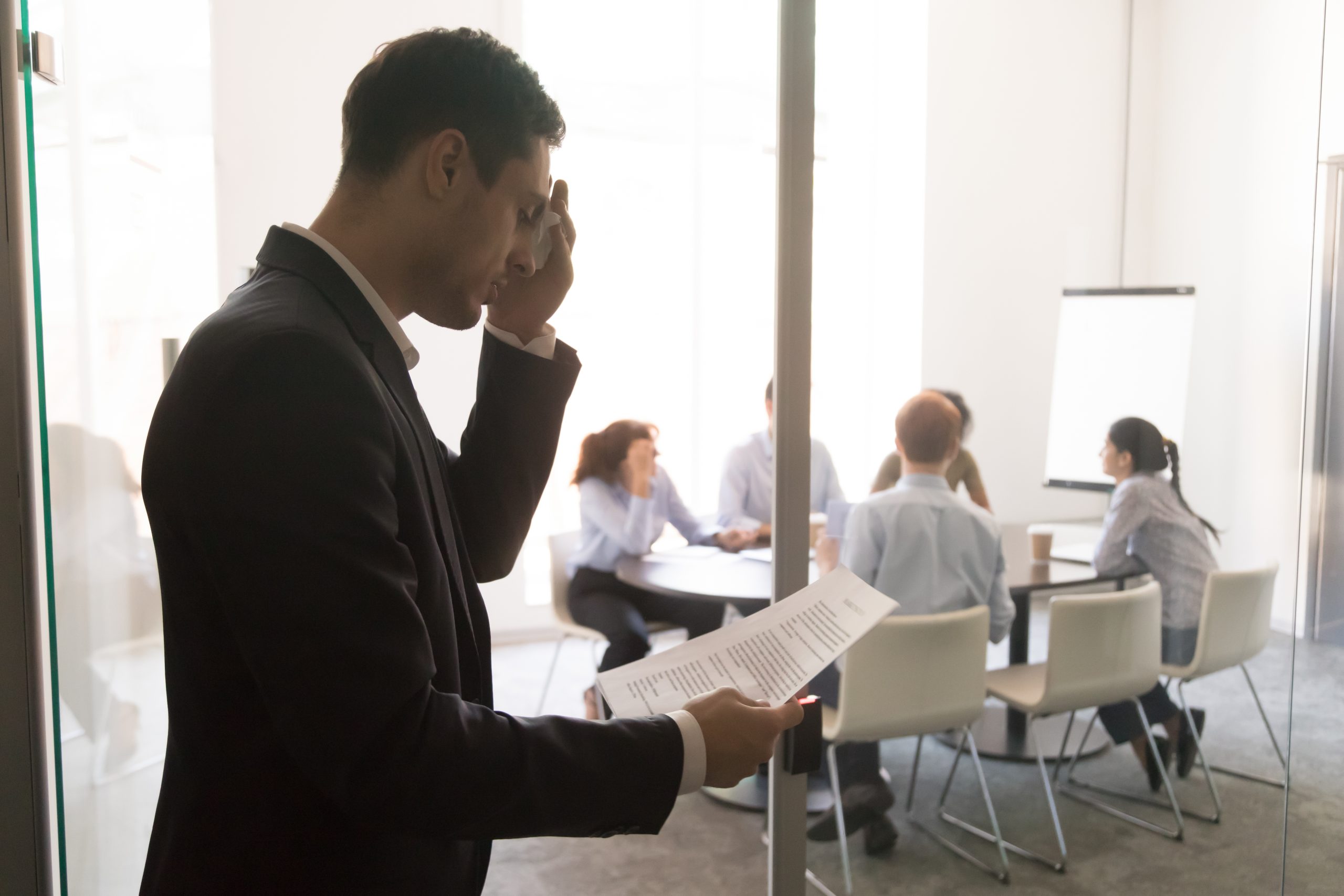 A businessman nervously prepares for a meeting with 5 other individuals who are waiting for his attendance.