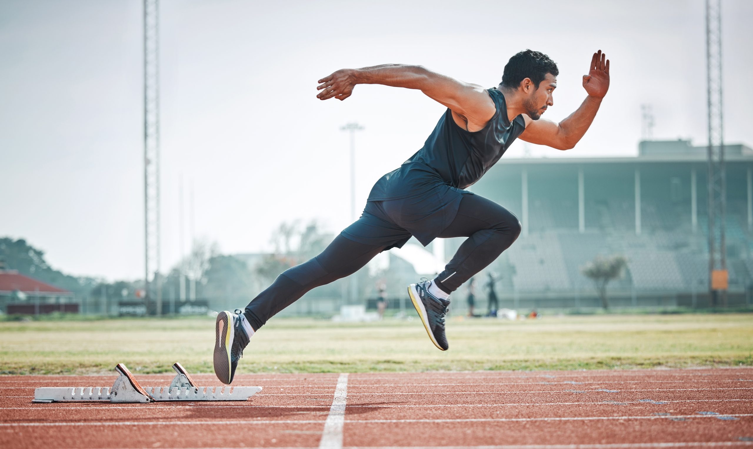 Male athlete at the start of a track run in an open stadium in peak running form and execution, focused on the finish line.