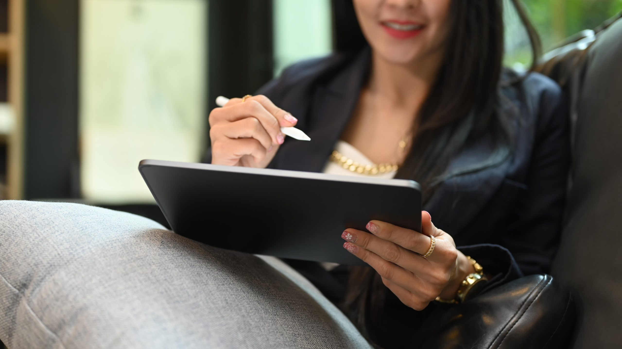 Smiling millennial woman using digital tablet while resting on couch at her personal office. Cropped shot.