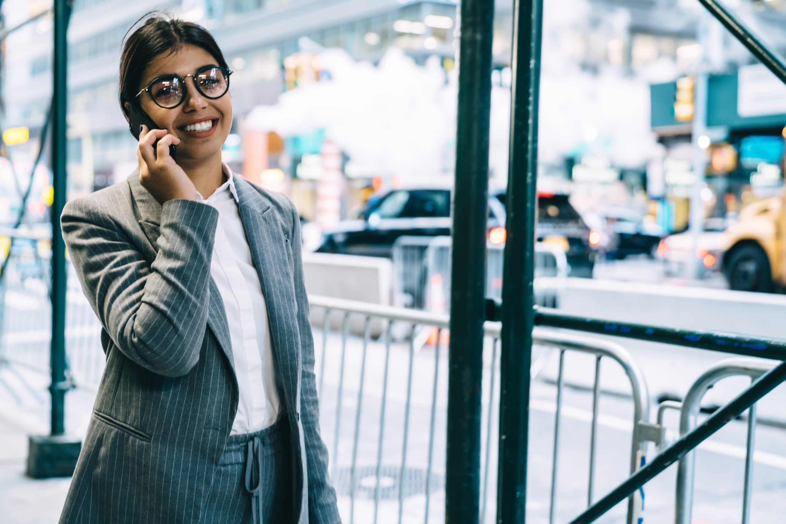 Half length portrait of cheerful female lawyer in trendy optical glasses smiling at camera during mobile smartphone conversation with business partner using her mobile device.